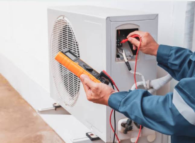 HVAC technician testing outdoor condenser wiring with a digital multimeter during an AC repair